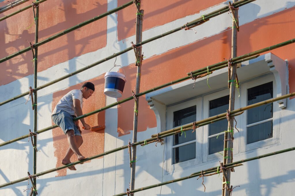 Asian painter on wooden scaffold is painting wall outside of the old house building